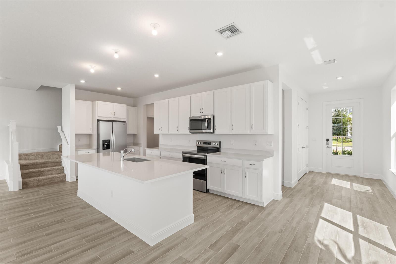 A bright kitchen features white cabinets, stainless steel appliances, a center island, and wood-look flooring — 1439 NW Corteal Way, Jensen Beach FL 34957, JENSEN BEACH, FL