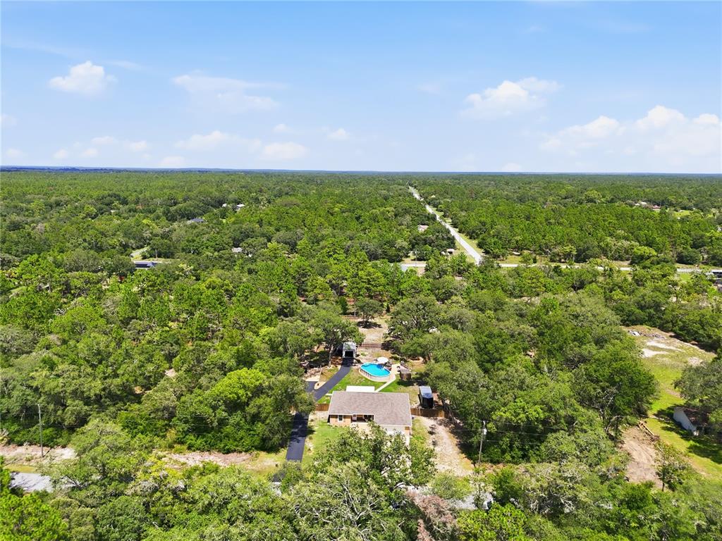 An aerial view shows a house with a pool surrounded by dense forest and trees — 4171 SW SHASTA COURT, DUNNELLON, FL