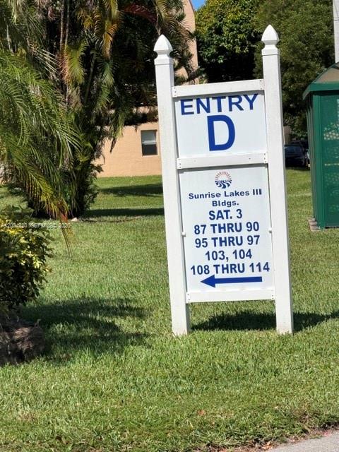 A white sign for Entry D at Sunrise Lakes III stands on a grassy lawn — SUNRISE, FL