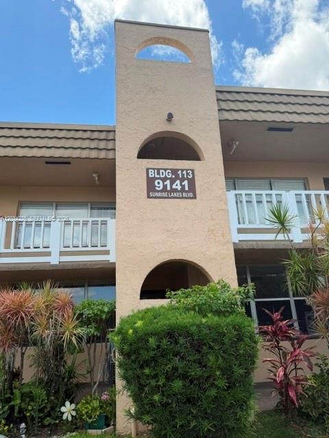 A tan stucco building exterior features a central tower with arched openings and signage — SUNRISE, FL