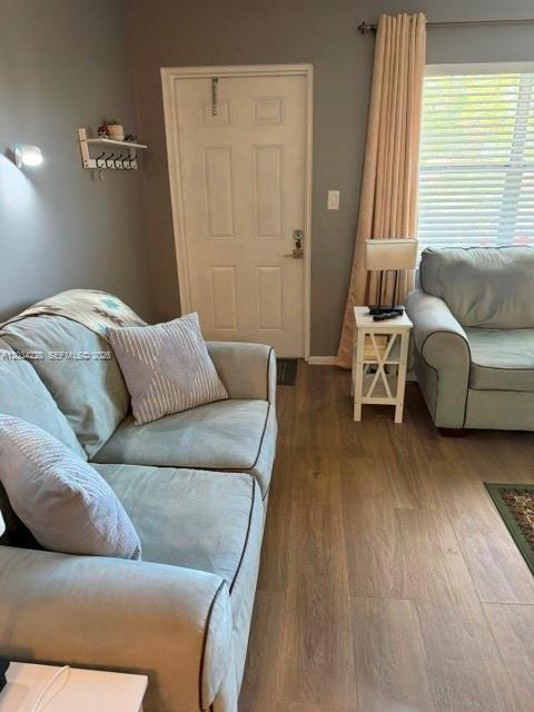A living room features light-colored sofas, wood-look flooring, and a door leading outside — SUNRISE, FL