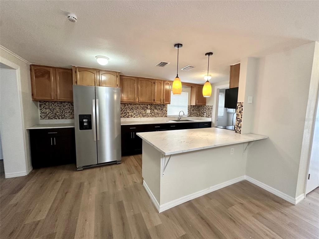 A kitchen features dark lower cabinets, wood-toned upper cabinets, a stainless refrigerator, and a breakfast bar — 13001 120TH STREET, SEMINOLE, FL