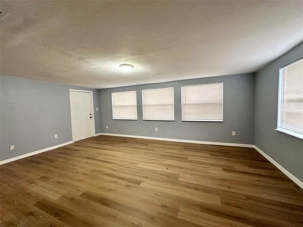 An empty room features light gray walls, wood-look flooring, a white door, and three windows — 13001 120TH STREET, SEMINOLE, FL