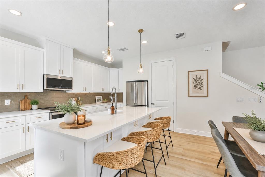 A modern kitchen features white cabinetry, a large quartz island with woven stools, and stainless appliances — 1911 W BEACH STREET, TAMPA, FL