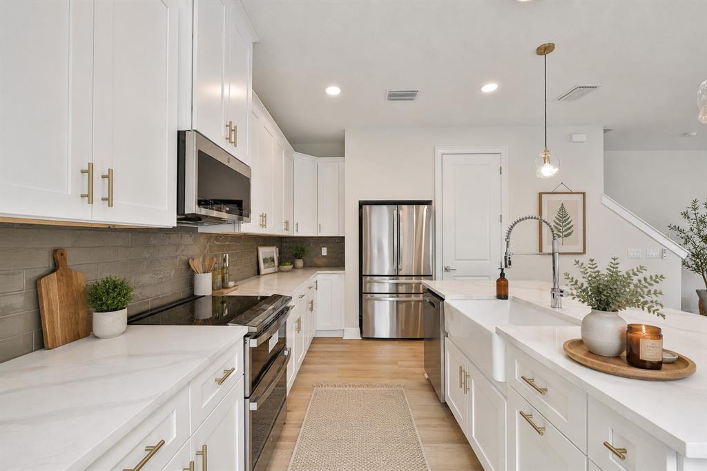 A modern kitchen features white cabinets, stainless steel appliances, a farmhouse sink, and wood flooring — 1911 W BEACH STREET, TAMPA, FL