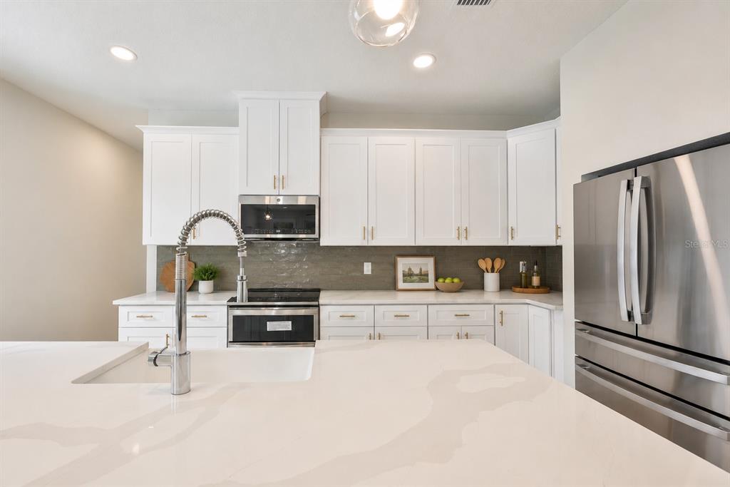A modern kitchen features white cabinets, quartz countertops, stainless steel appliances, and a gray backsplash — 1911 W BEACH STREET, TAMPA, FL