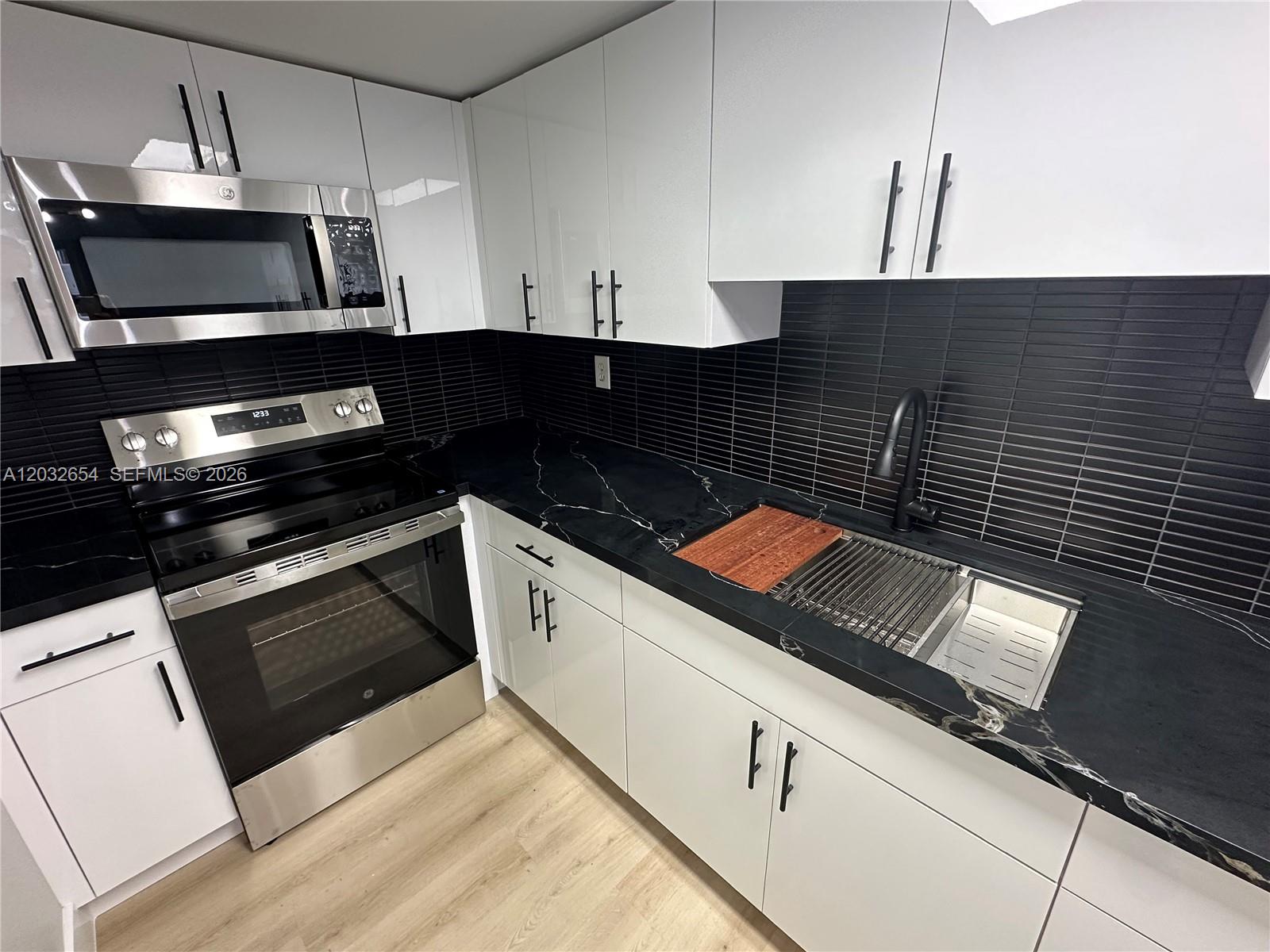 A kitchen features white cabinets, black marble countertops, a stainless steel stove, and black tile backsplash — 10090 NW 80th Ct # 1325, Hialeah Gardens FL 33016, HIALEAH GARDENS, FL