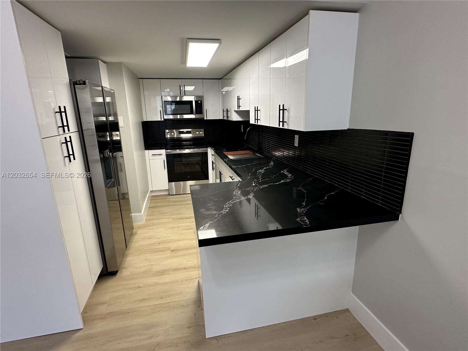 A modern kitchen features white cabinets, black marble-style countertops, and a black tiled backsplash — 10090 NW 80th Ct # 1325, Hialeah Gardens FL 33016, HIALEAH GARDENS, FL