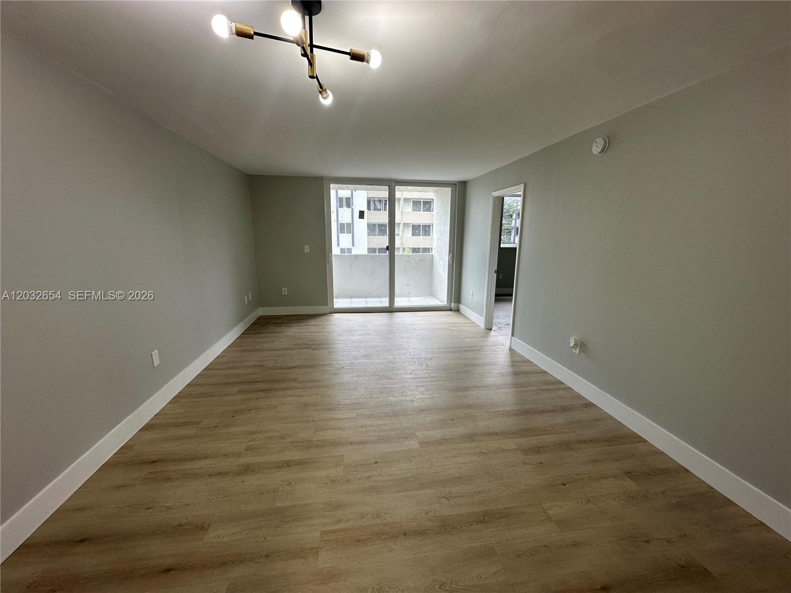 An empty living room features light-colored wood-look flooring, gray walls, and a sliding glass door — 10090 NW 80th Ct # 1325, Hialeah Gardens FL 33016, HIALEAH GARDENS, FL