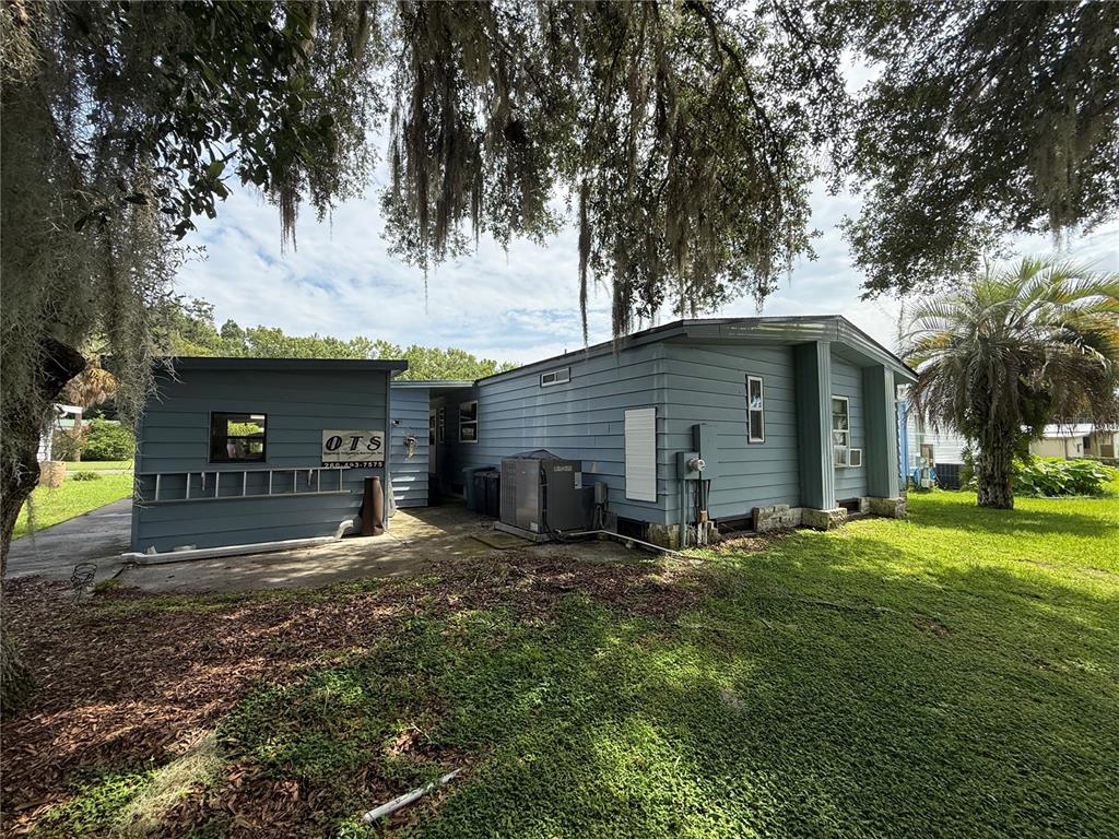A blue-sided house with a concrete patio and an outdoor HVAC unit under trees — 802 ROBIN LANE, WILDWOOD, FL