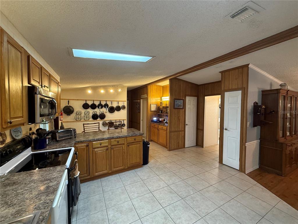 A kitchen features wood cabinets, a tile floor, a central island, and a hanging pan rack — 802 ROBIN LANE, WILDWOOD, FL
