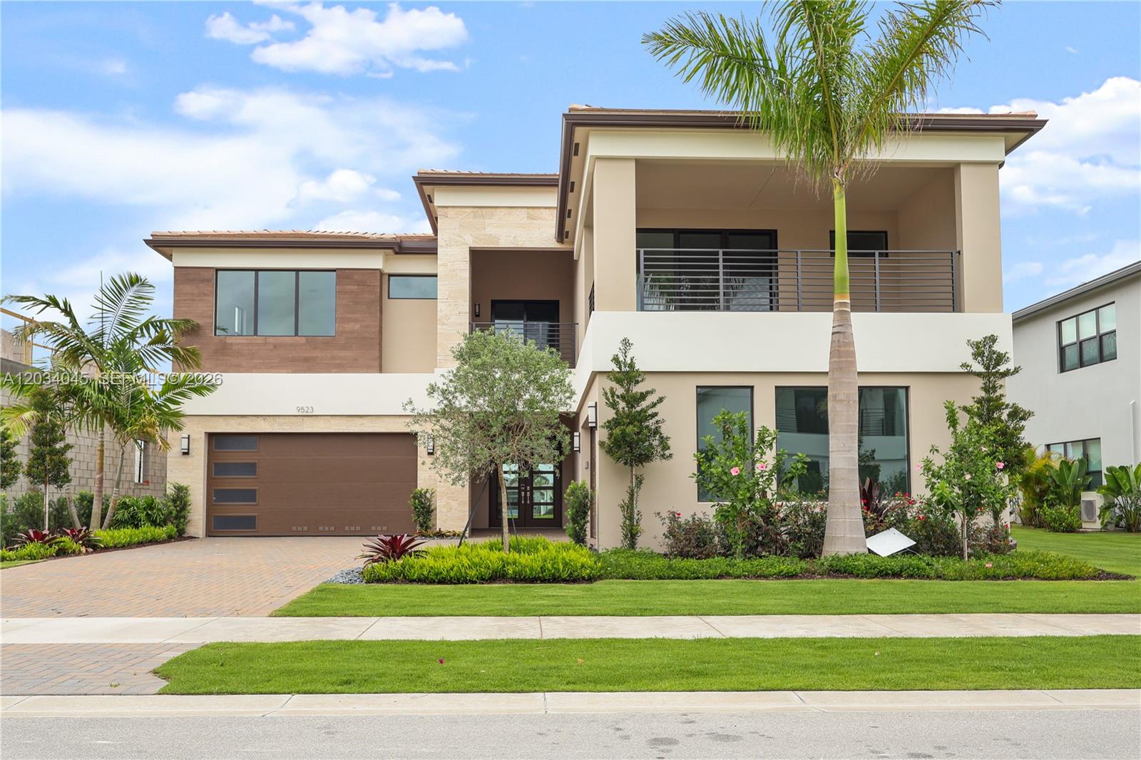 A two-story modern house features a brown garage, stone accents, and a second-floor balcony — 9523 Royal Woods Mnr, Boca Raton FL 33434, BOCA RATON, FL