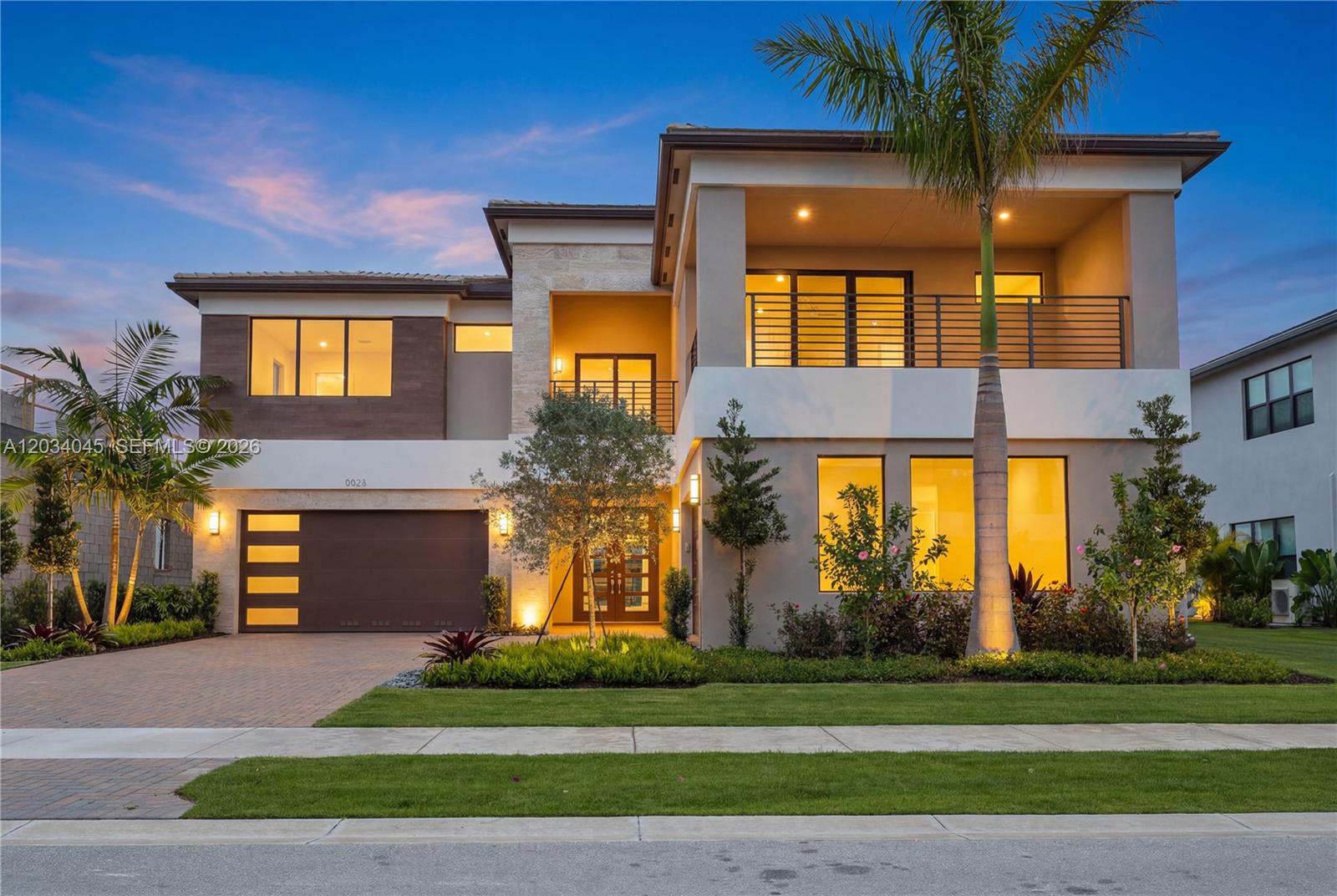 A modern two-story house features a garage, a balcony, and landscaped front yard at dusk — 9523 Royal Woods Mnr, Boca Raton FL 33434, BOCA RATON, FL