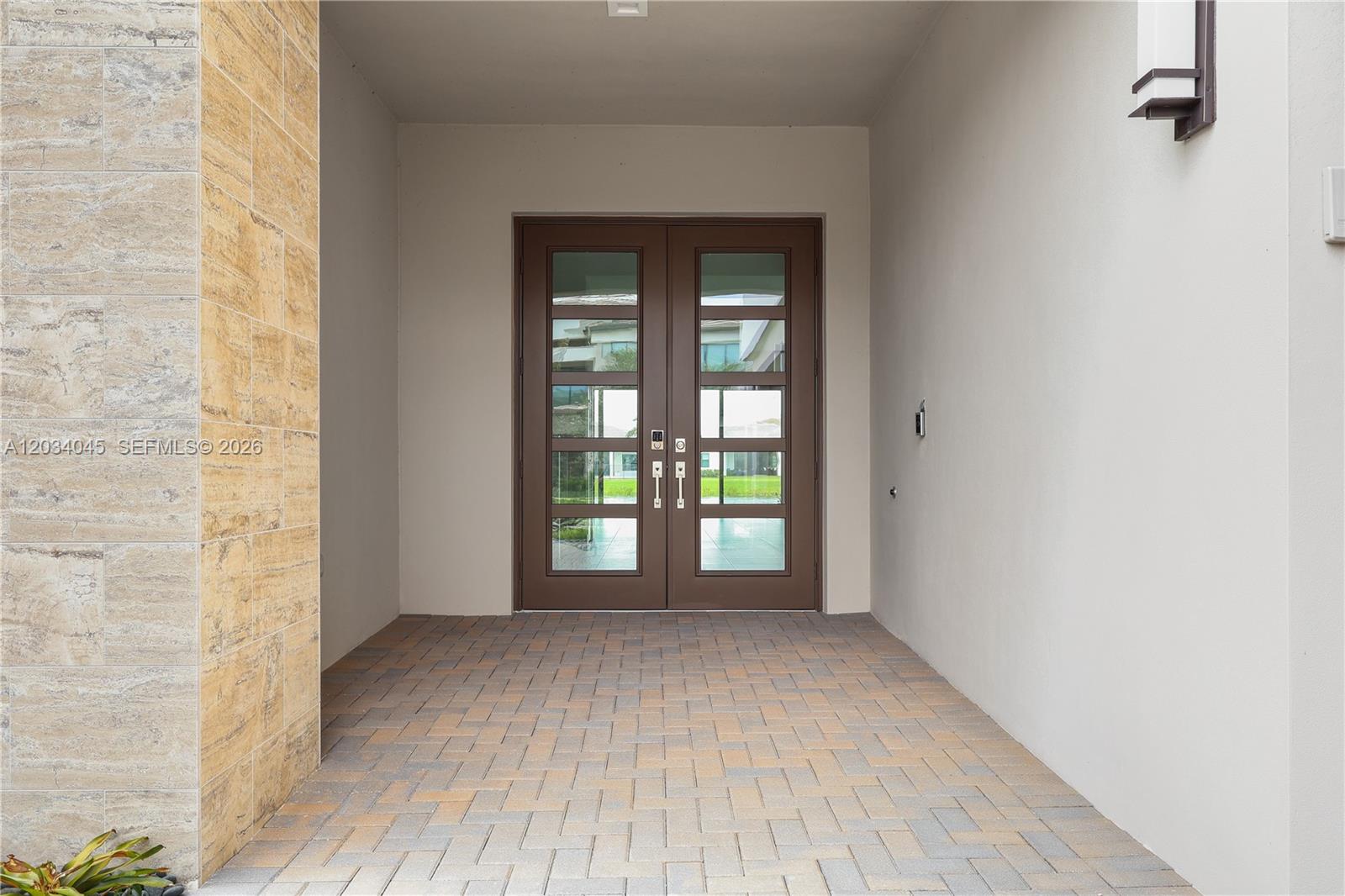 A covered entryway features a double glass door, stone-tiled wall, and paved flooring — 9523 Royal Woods Mnr, Boca Raton FL 33434, BOCA RATON, FL