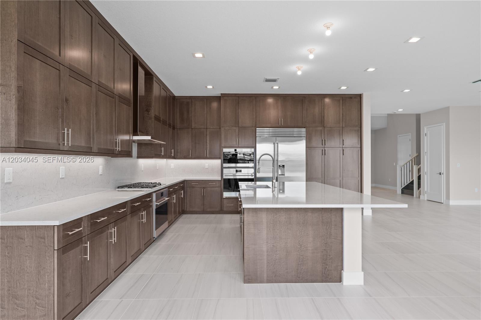 A modern kitchen features dark wood cabinetry, white quartz countertops, and stainless steel appliances — 9523 Royal Woods Mnr, Boca Raton FL 33434, BOCA RATON, FL