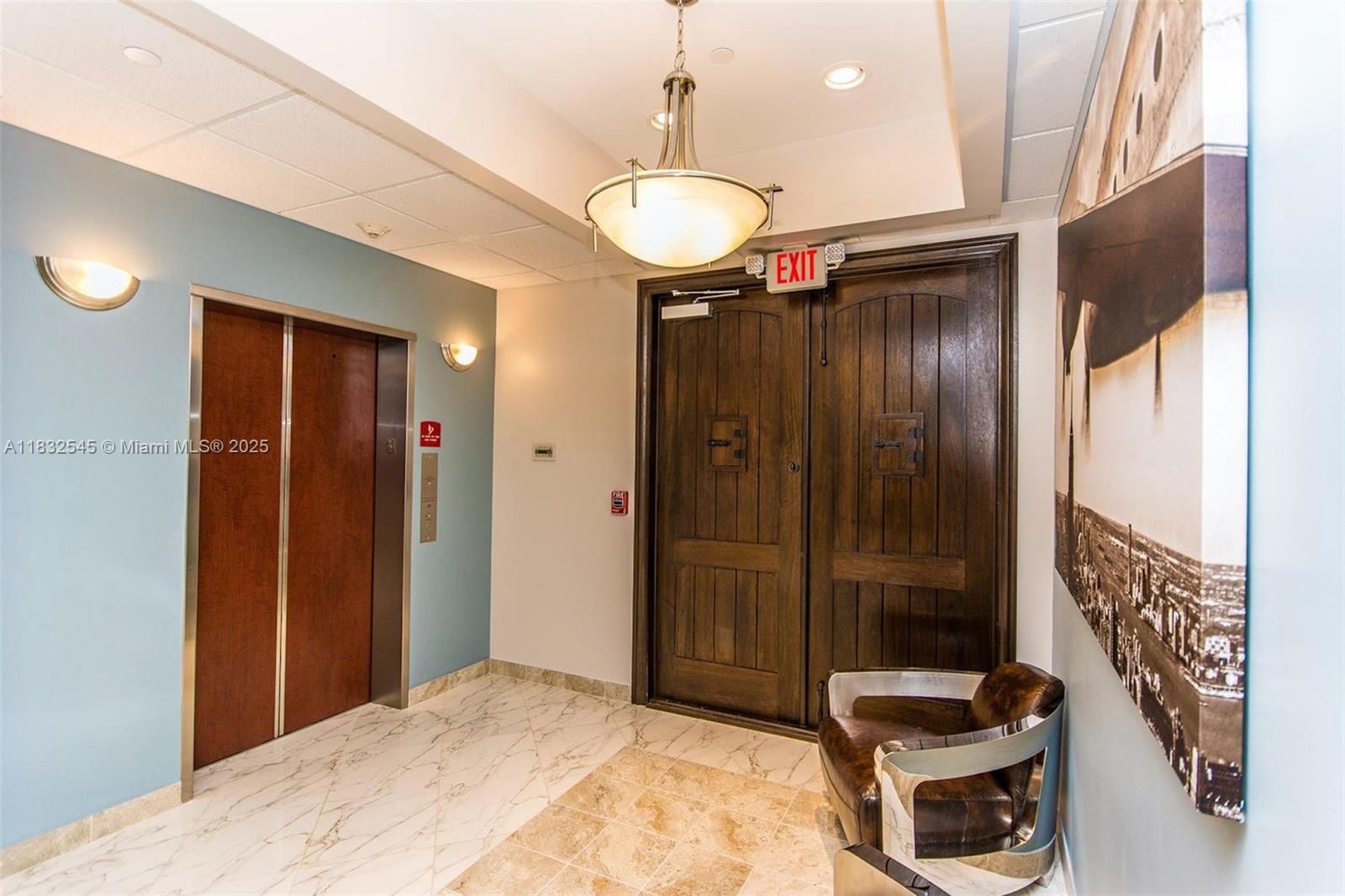 This interior lobby features an elevator, double wooden doors, a leather chair, and tile flooring — 1555 Bonaventure Blvd # 2019, Weston FL 33326, WESTON, FL