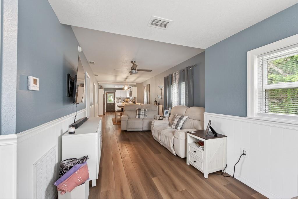 A living room with blue walls, white wainscoting, wood-look flooring, and a view into the kitchen — 6101 ANNA AVENUE, GIBSONTON, FL