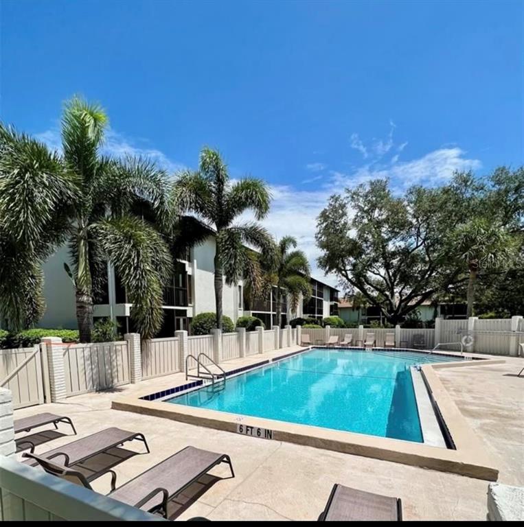 An outdoor swimming pool is surrounded by lounge chairs, palm trees, and a white fence — 7203 CURTISS AVENUE UNIT 1A, SARASOTA, FL