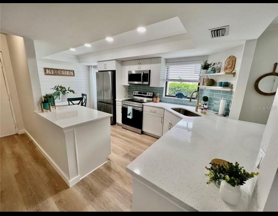 A modern kitchen features white cabinets, quartz countertops, stainless steel appliances, and light wood flooring — 7203 CURTISS AVENUE UNIT 1A, SARASOTA, FL