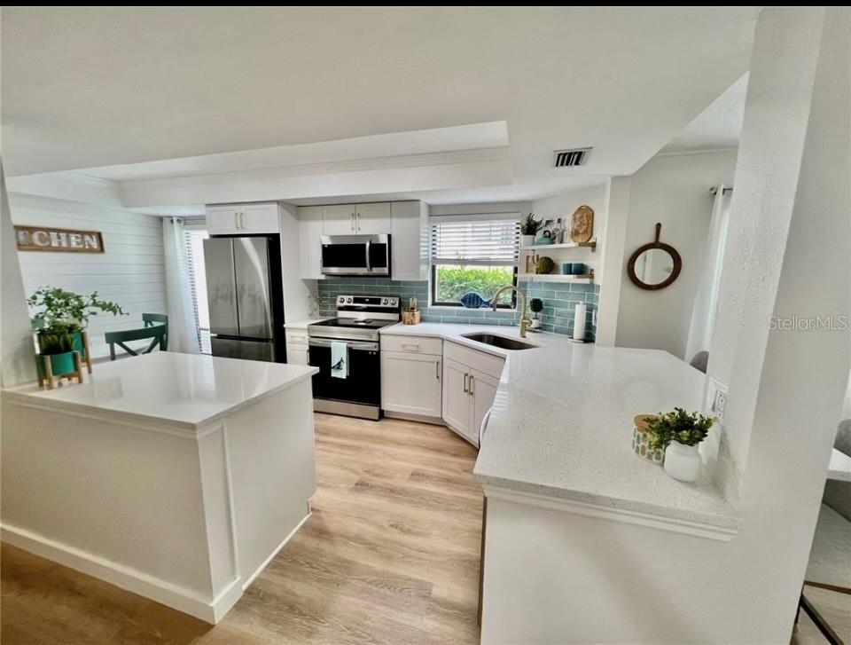A modern kitchen features white cabinetry, quartz countertops, stainless steel appliances, and a central island — 7203 CURTISS AVENUE UNIT 1A, SARASOTA, FL