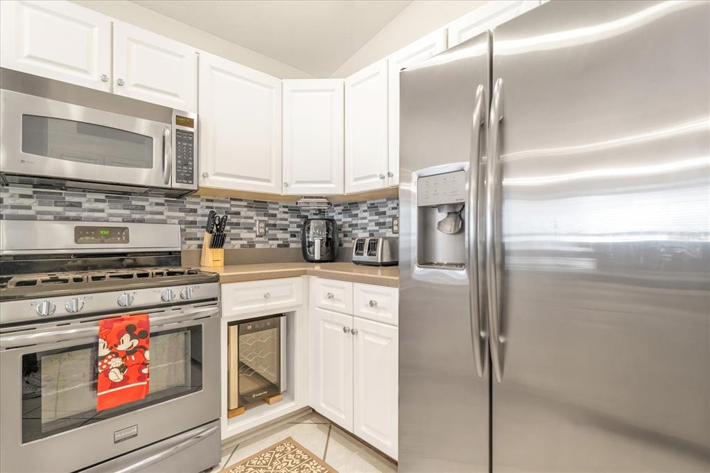 A kitchen features white cabinets, stainless steel appliances, a tiled backsplash, and a wine cooler — 111 PINEWOOD DRIVE, DAVENPORT, FL