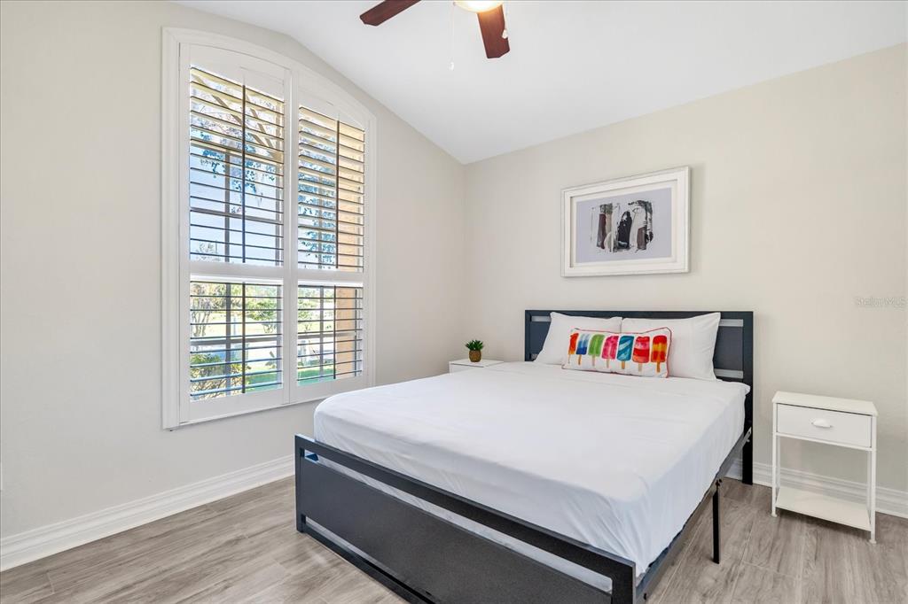 A bedroom features a bed with a dark frame, white bedding, and a window with shutters — 111 PINEWOOD DRIVE, DAVENPORT, FL
