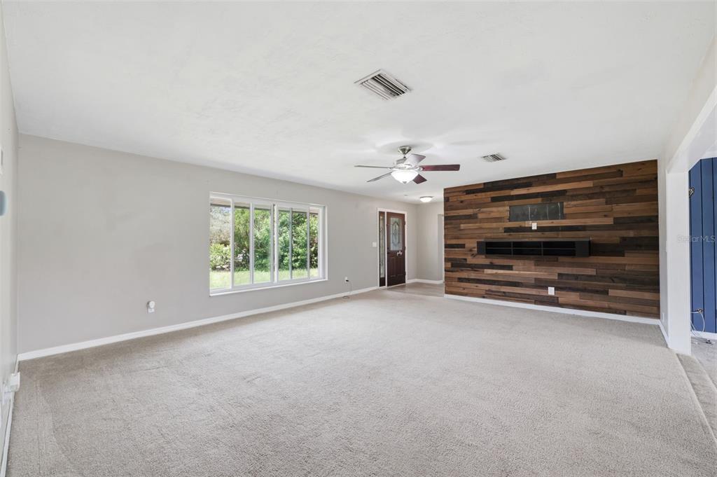 A living room features beige carpeting, light gray walls, and a wood-paneled accent wall — 459 SAVOY COURT, SPRING HILL, FL