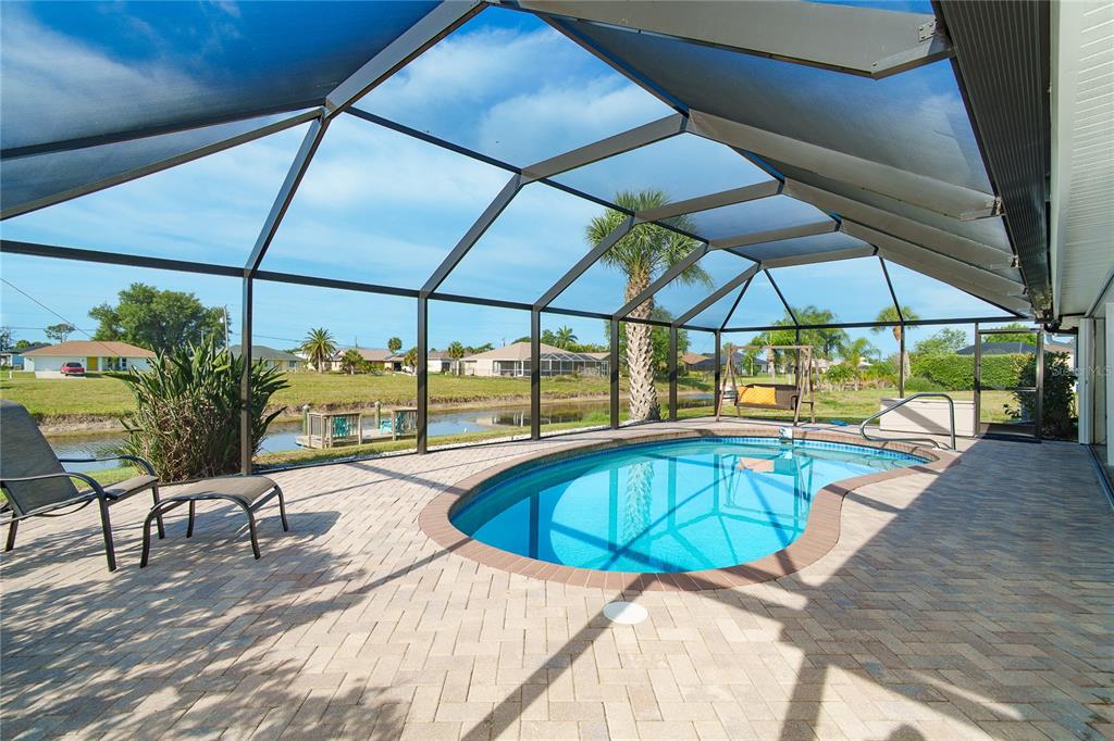 A screened-in pool patio with brick pavers overlooks a canal and residential neighborhood — 99 BUNKER ROAD, ROTONDA WEST, FL