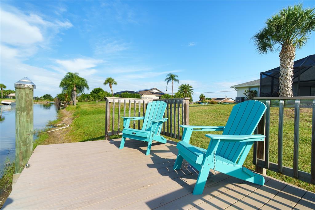 Two turquoise Adirondack chairs sit on a wooden deck overlooking a canal and grassy yard — 99 BUNKER ROAD, ROTONDA WEST, FL