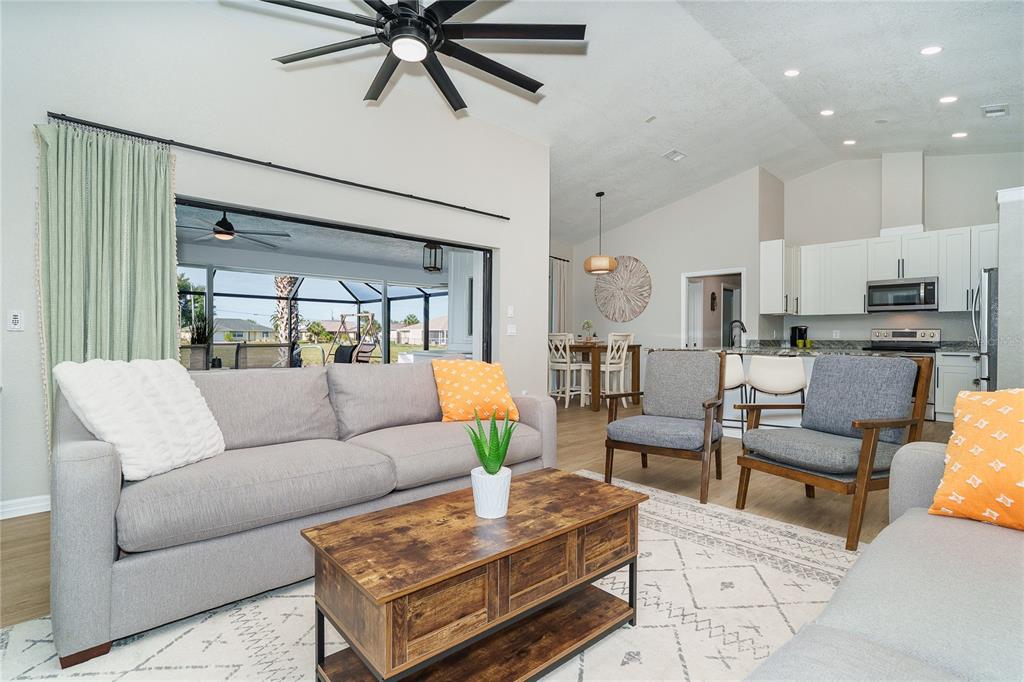 A living room with a grey sofa, two armchairs, a coffee table, and an open kitchen — 99 BUNKER ROAD, ROTONDA WEST, FL