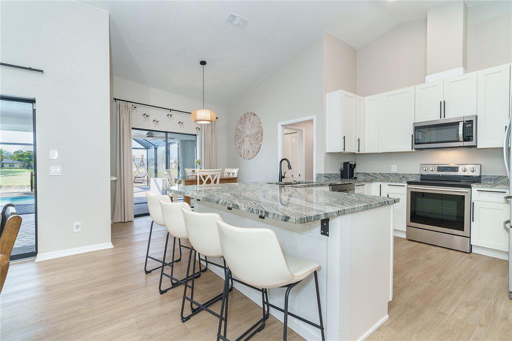 A kitchen features white cabinets, granite countertops, a center island with bar seating, and flooring — 99 BUNKER ROAD, ROTONDA WEST, FL