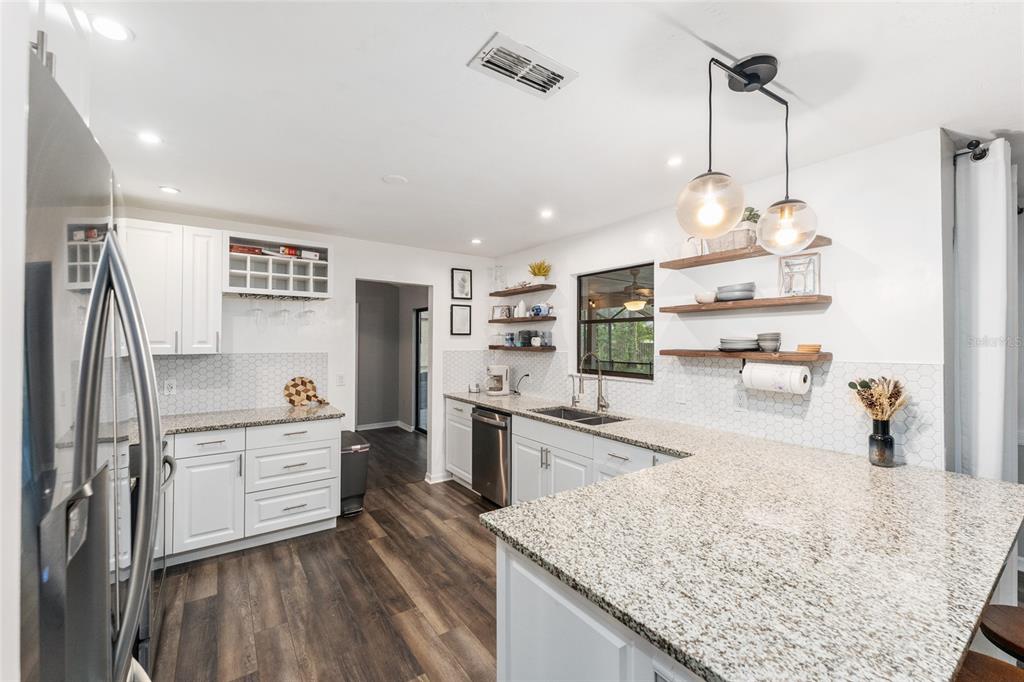 A kitchen features white cabinets, granite countertops, open shelving, and wood-look flooring — 8005 SW 47TH COURT, GAINESVILLE, FL