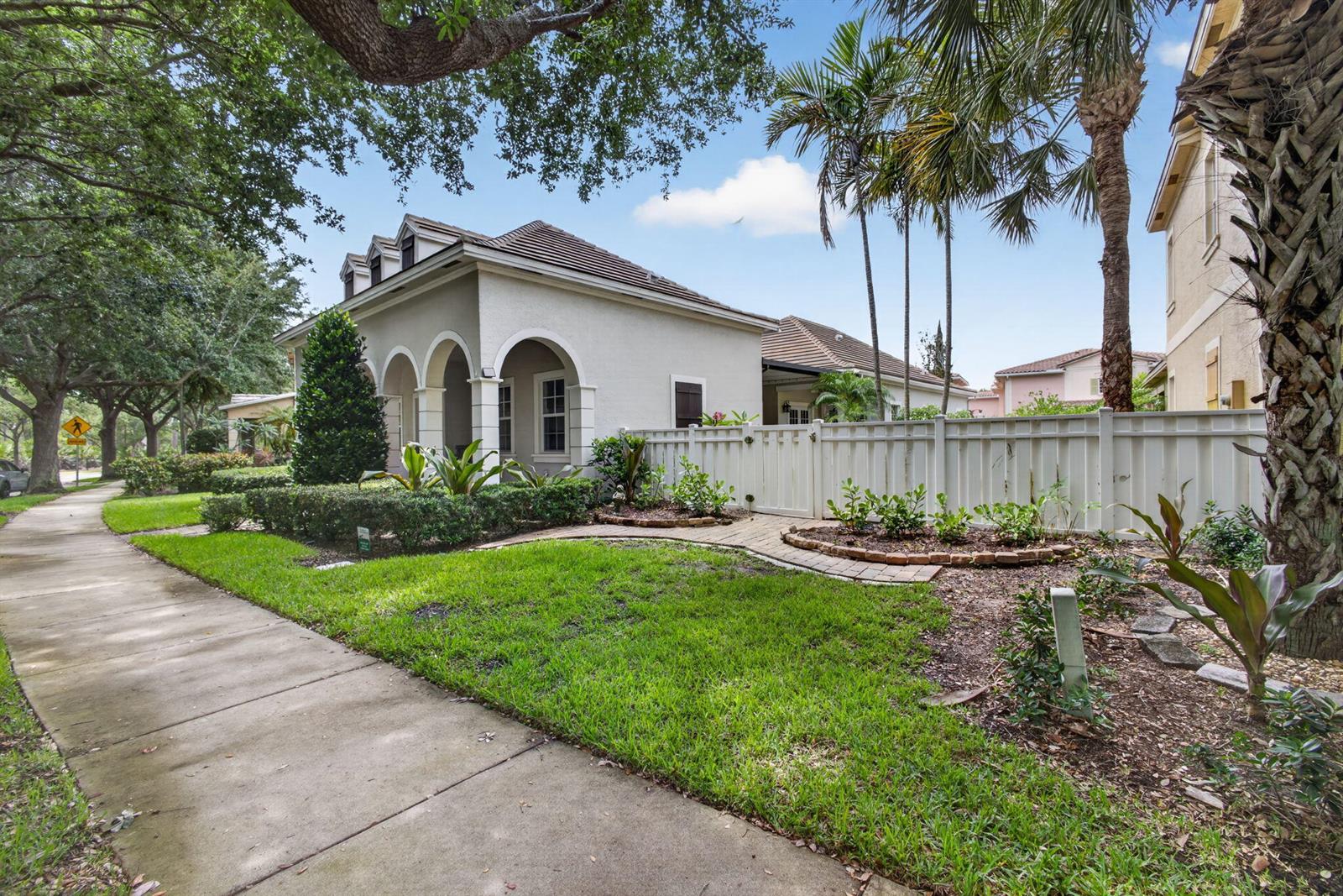 A light-colored house with arched entryways sits behind a white fence next to a sidewalk — 127 Arklow Avenue, Jupiter FL 33458, JUPITER, FL