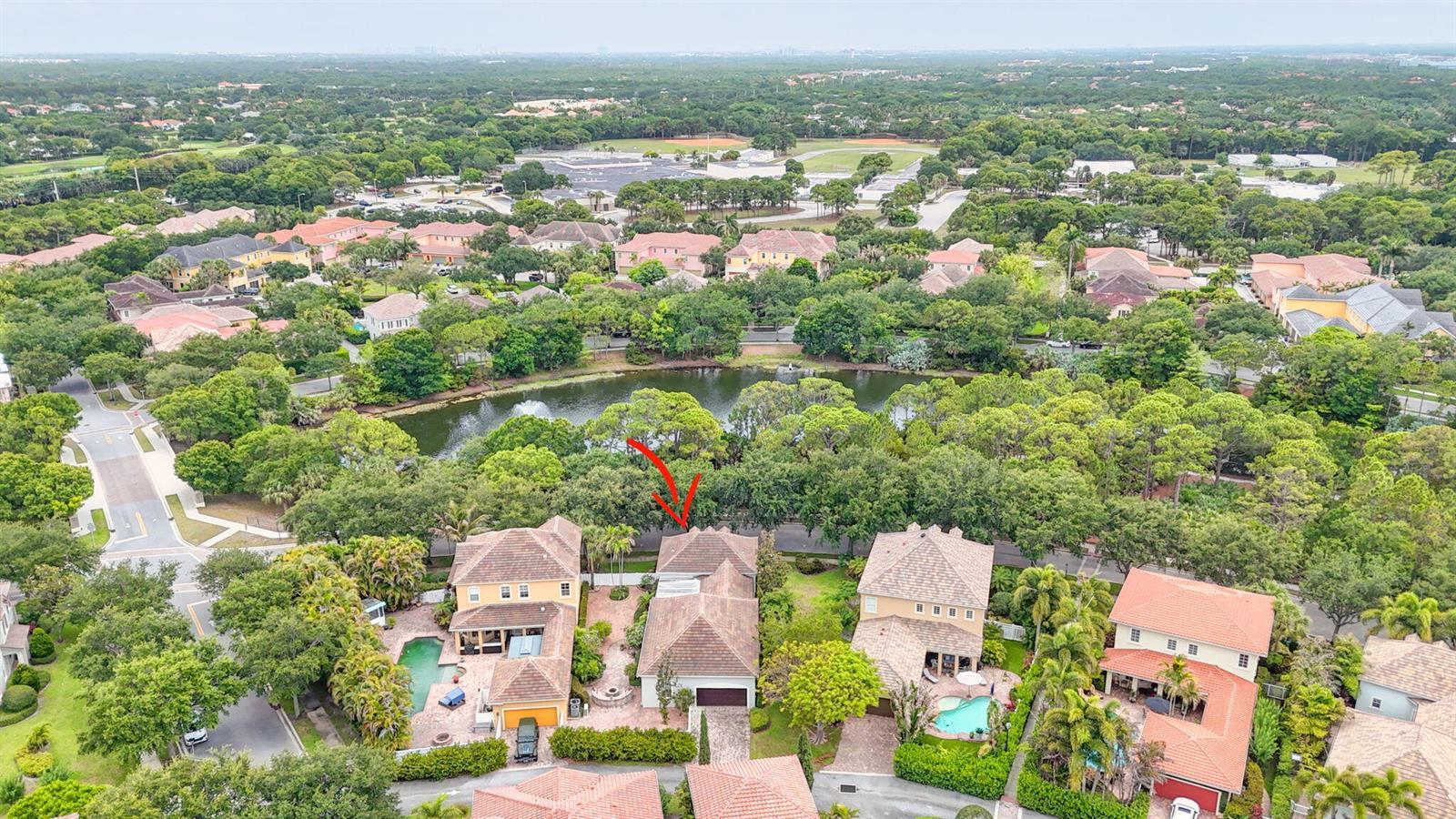An aerial view shows a residential neighborhood with houses, a central lake, and trees — 127 Arklow Avenue, Jupiter FL 33458, JUPITER, FL