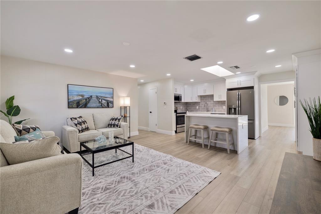 An open-concept living room and kitchen featuring light wood flooring and white cabinetry — 490 82ND AVENUE, ST PETE BEACH, FL