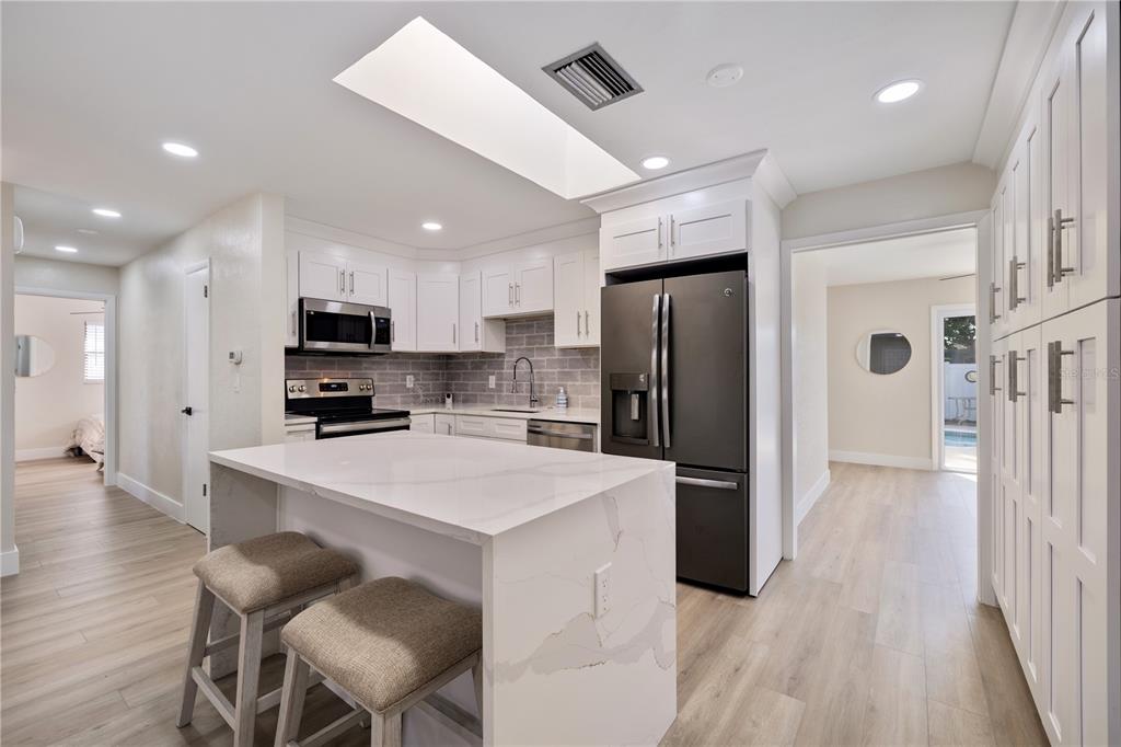 A modern kitchen features white cabinets, a quartz island with seating, and stainless steel appliances — 490 82ND AVENUE, ST PETE BEACH, FL