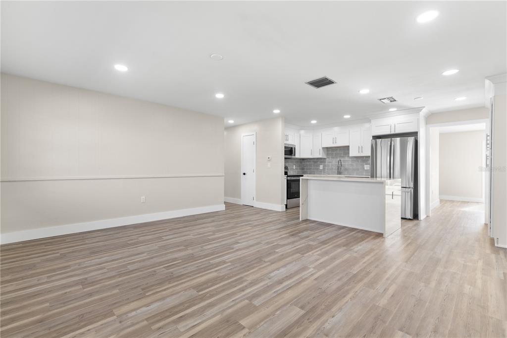 An open-concept living area features light wood-look flooring, white kitchen cabinets, and stainless appliances — 490 82ND AVENUE, ST PETE BEACH, FL