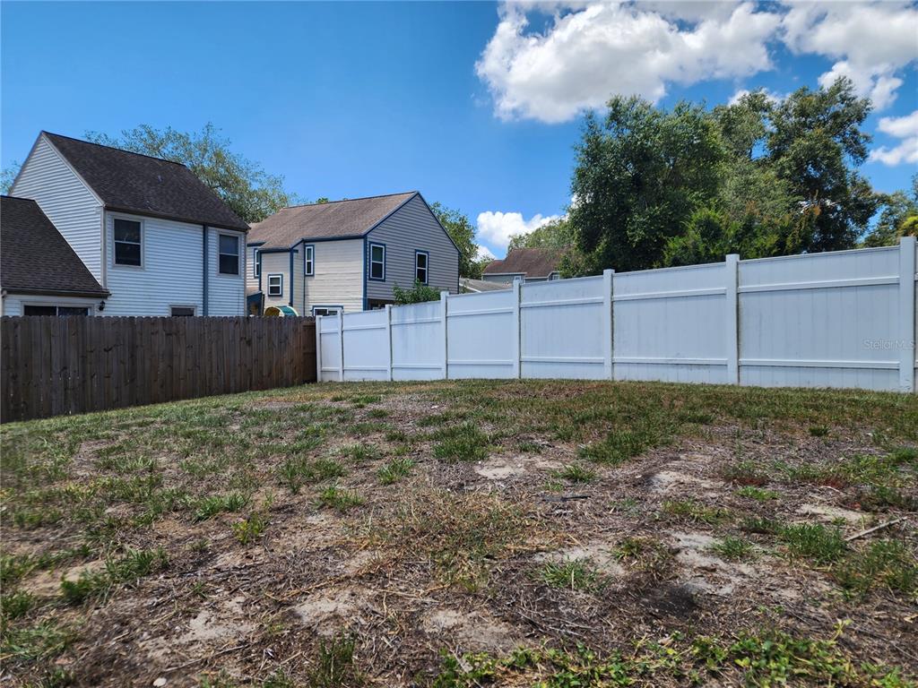 A backyard features a patch of grass and dirt enclosed by white and brown fences — 7507 WAKULLA DRIVE, TEMPLE TERRACE, FL