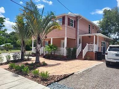 A two-story pink house with a porch and a paved driveway sits under a blue sky — 232 CYPRESS STREET, TARPON SPRINGS, FL