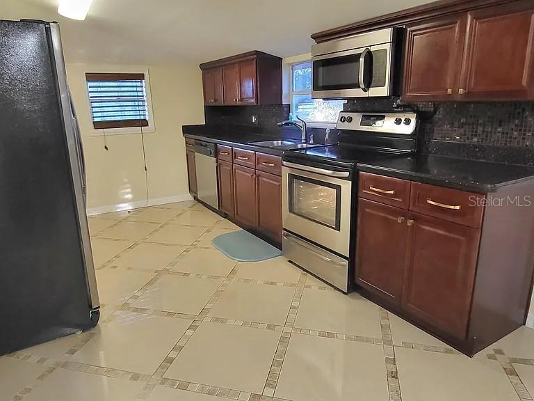 A kitchen features dark wood cabinets, stainless steel appliances, and light-colored tiled flooring — 232 CYPRESS STREET, TARPON SPRINGS, FL