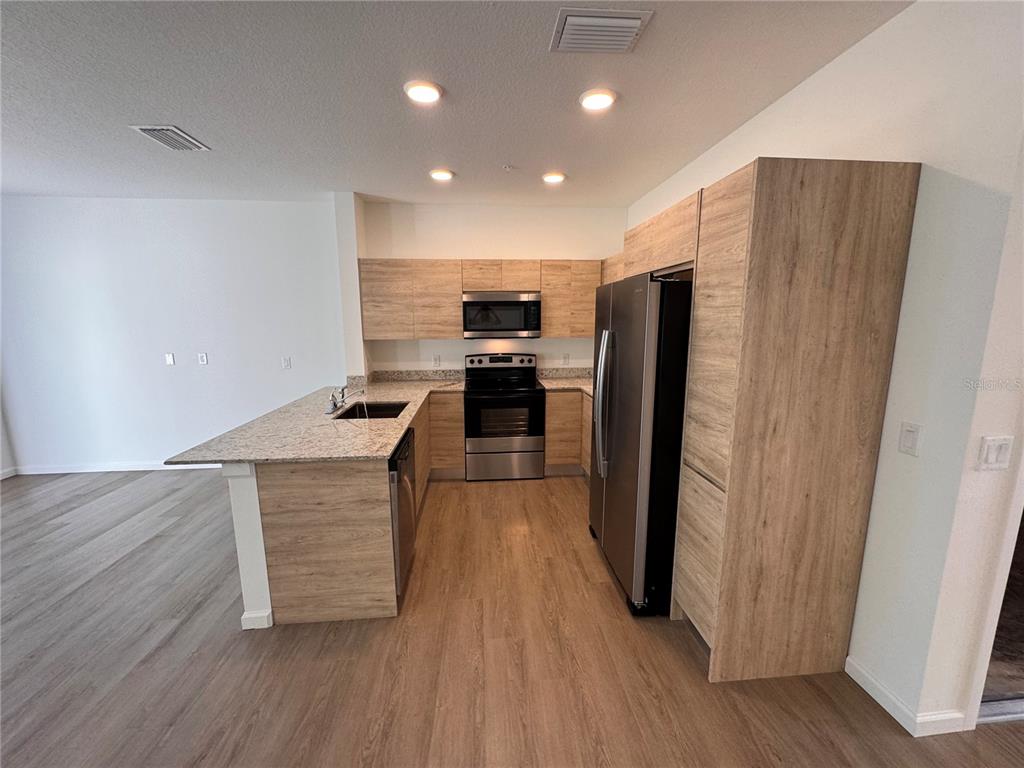A kitchen features light wood cabinets, stainless steel appliances, and a granite-topped peninsula — 1209 SOUTHSTATION PLACE UNIT 303, ORLANDO, FL