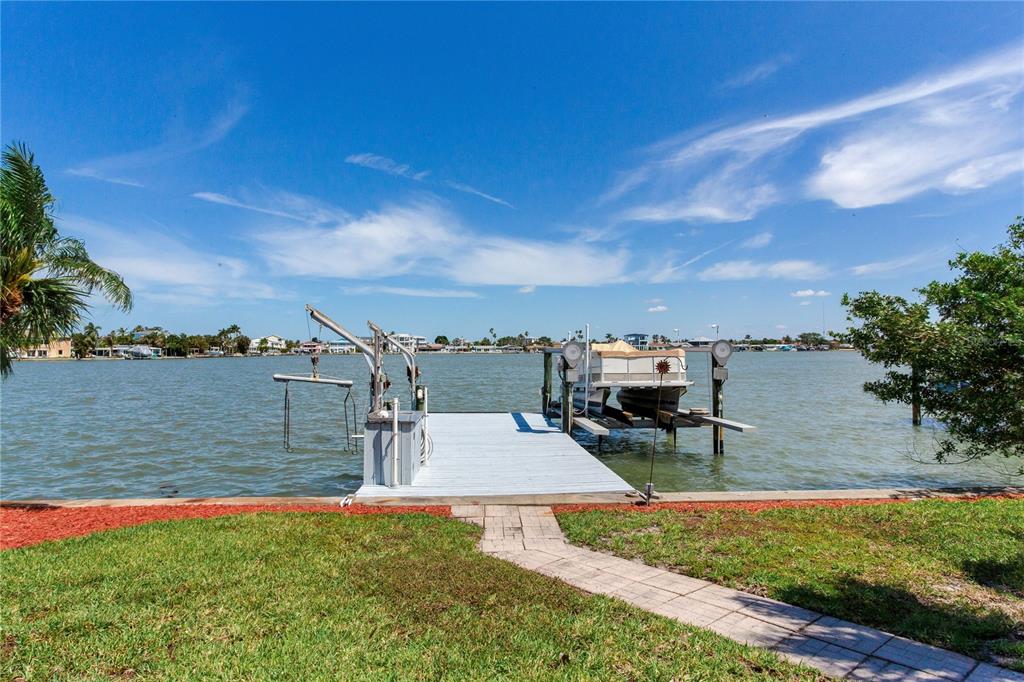 A wooden dock with a boat lift extends into a bay from a grassy yard — 324 173RD AVENUE E, NORTH REDINGTON BEACH, FL
