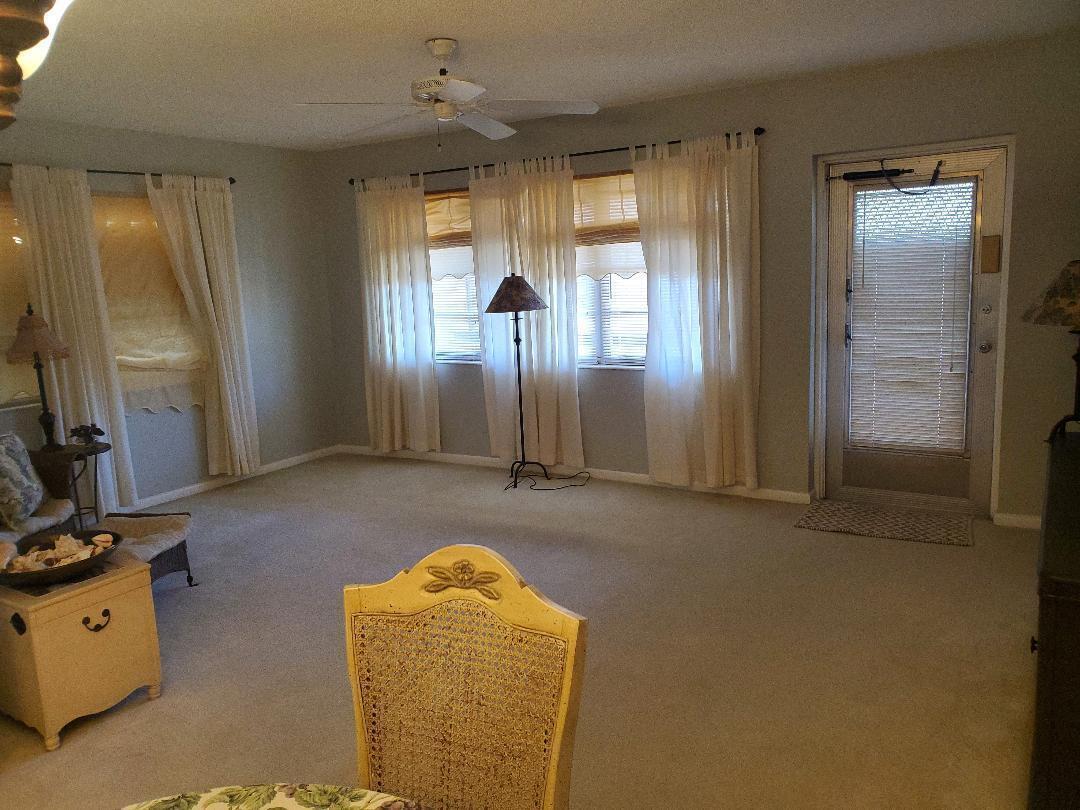 A living room features beige carpeting, light gray walls, white curtains, and a ceiling fan — 73 Andover C, West Palm Beach FL 33417, WEST PALM BEACH, FL