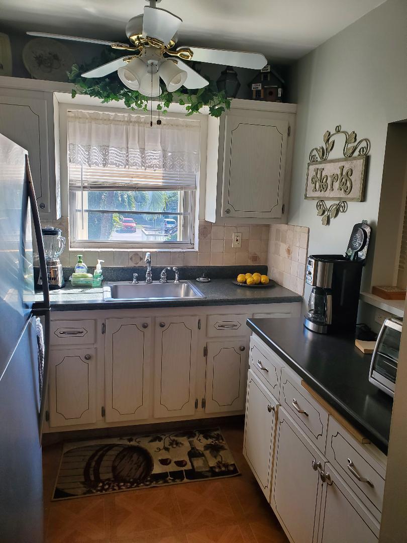 A kitchen with white cabinets, dark countertops, a window over the sink, and a ceiling fan — 73 Andover C, West Palm Beach FL 33417, WEST PALM BEACH, FL