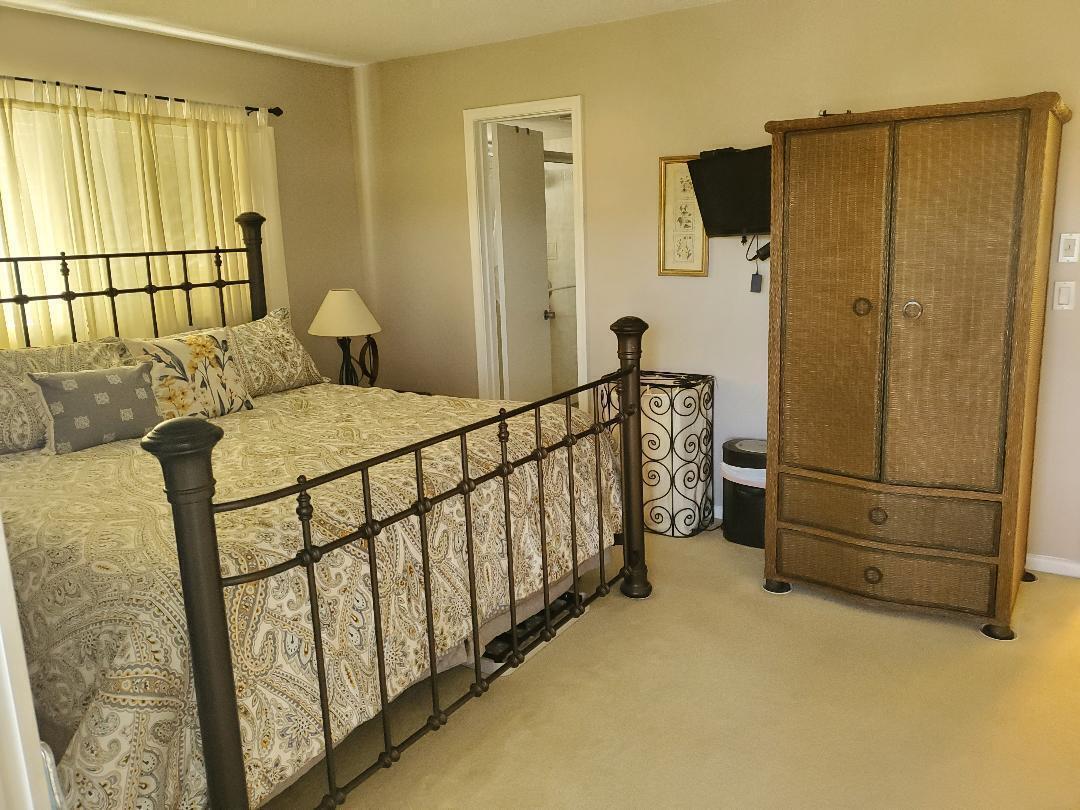 A bedroom features a metal-framed bed, a wicker armoire, and a doorway to a bathroom — 73 Andover C, West Palm Beach FL 33417, WEST PALM BEACH, FL