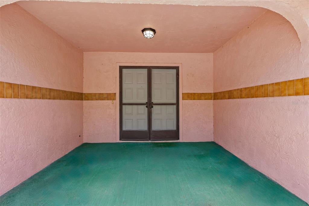 A covered porch with pink stucco walls, a horizontal tile border, and a green floor — 505 VILLAGE OAK DRIVE, TARPON SPRINGS, FL