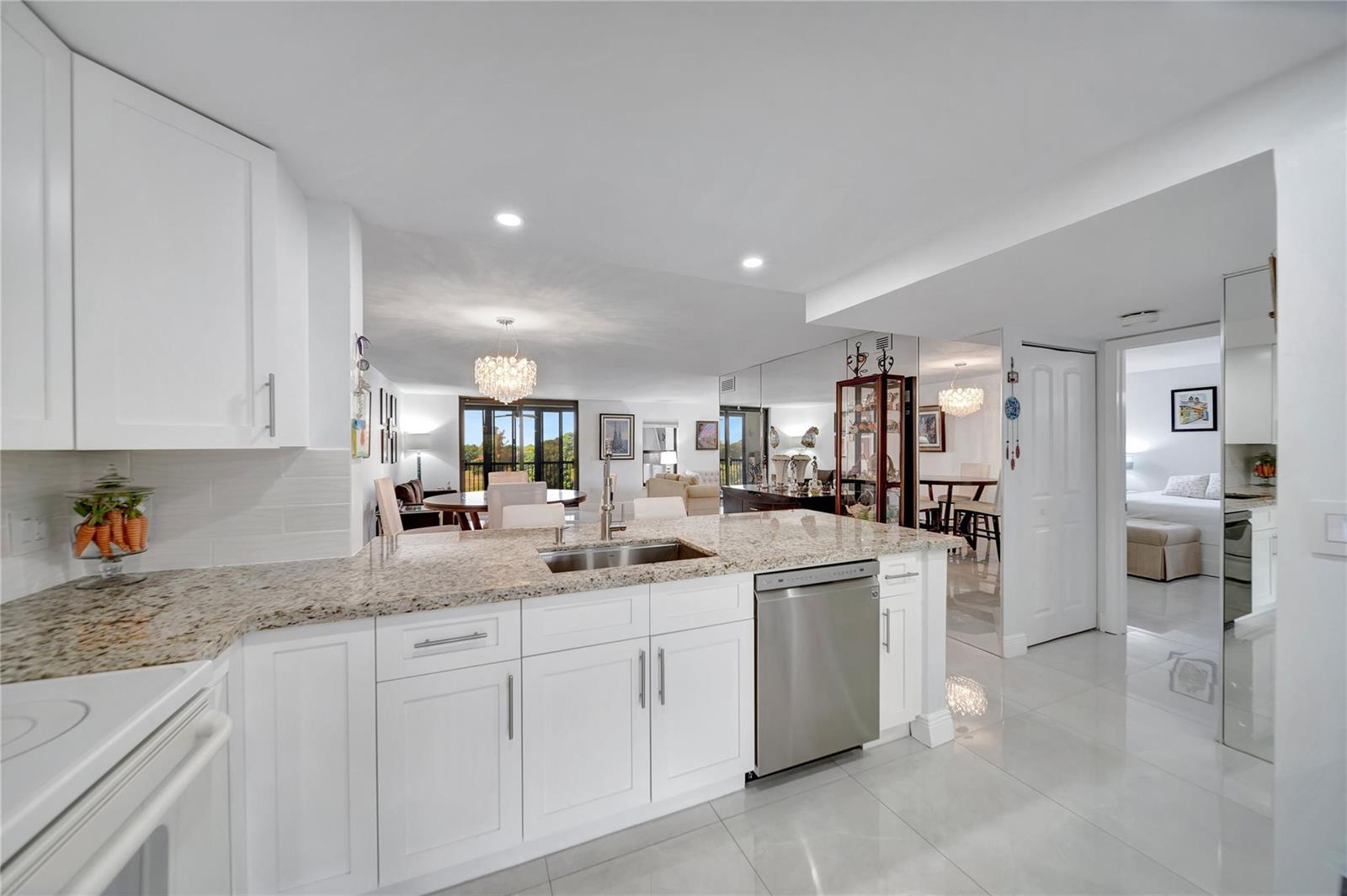 A white kitchen with granite countertops overlooks a dining area and living room — 3521 Environ Boulevard # B410, Lauderhill FL 33319, LAUDERHILL, FL