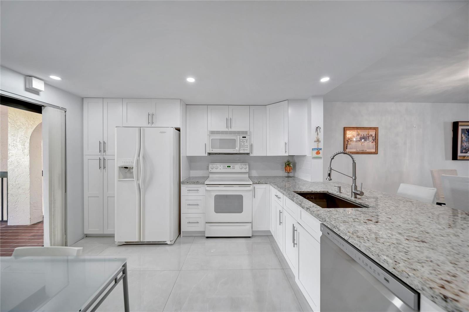 A white kitchen features granite countertops, stainless steel appliances, and tile flooring — 3521 Environ Boulevard # B410, Lauderhill FL 33319, LAUDERHILL, FL