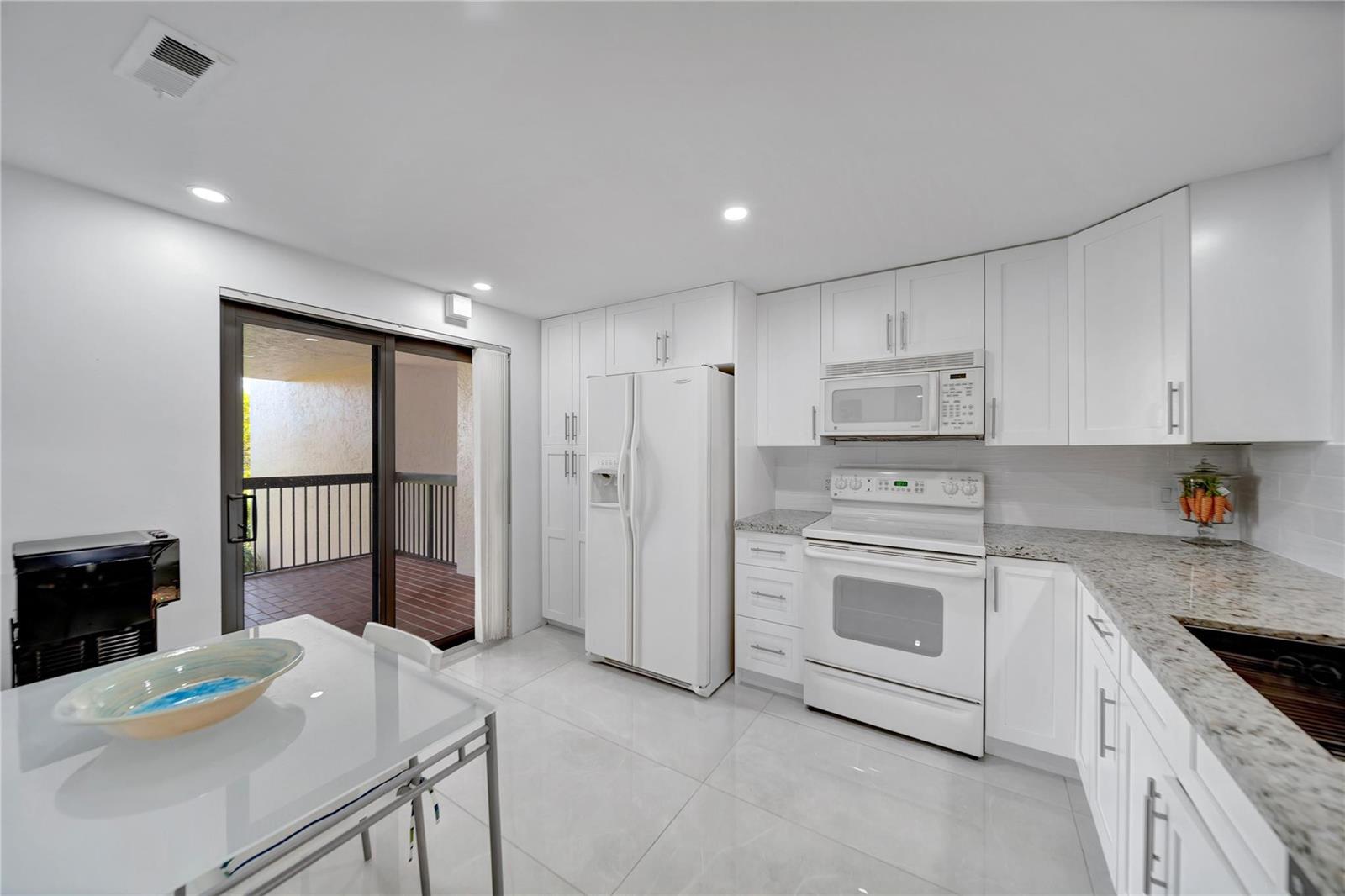 A kitchen with white cabinets, granite countertops, white appliances, and a sliding glass door — 3521 Environ Boulevard # B410, Lauderhill FL 33319, LAUDERHILL, FL