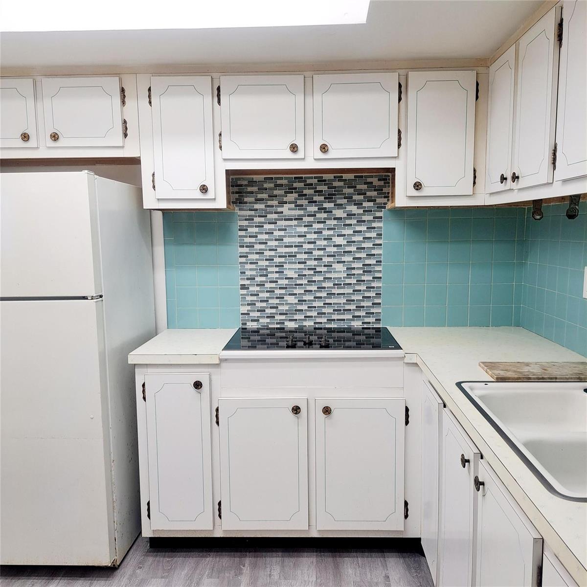 A kitchen features white cabinets, a glass cooktop, and a blue tiled backsplash — 6730 Arbor Drive # 210, Miramar FL 33023, MIRAMAR, FL
